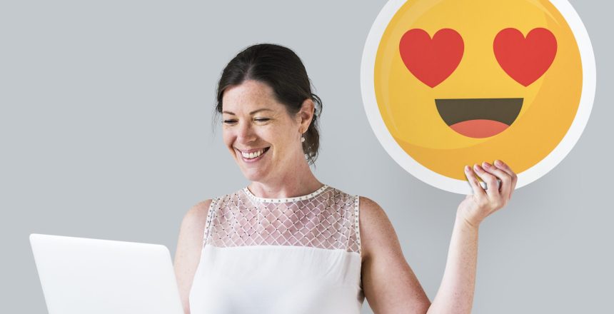 Woman holding a heart eyes emoticon and a laptop